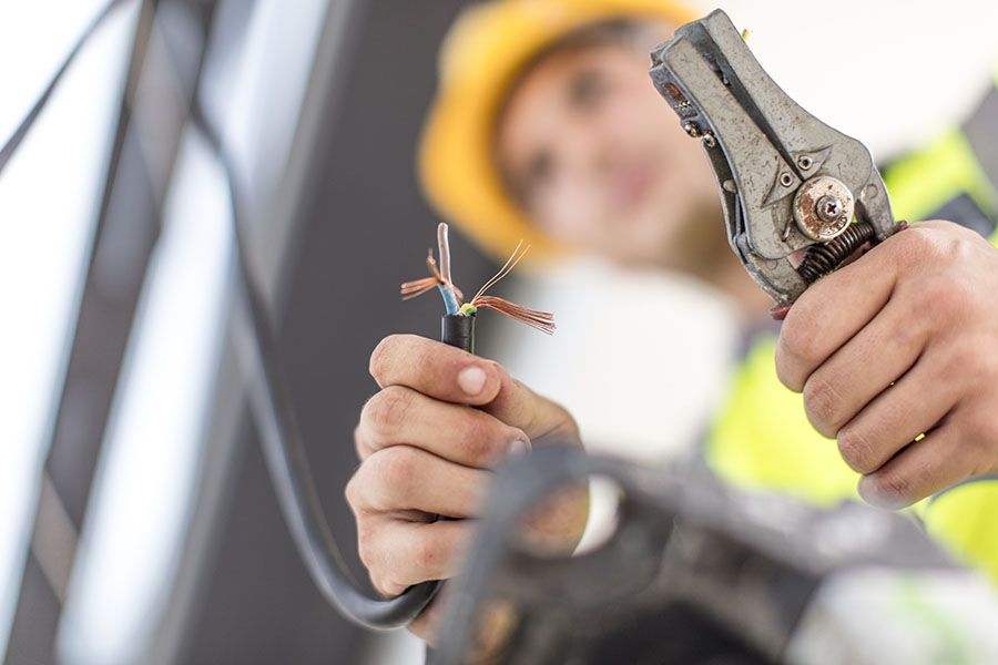 A person in a safety vest uses pliers to work on exposed electrical wires, demonstrating a focus on wiring and electrical tasks.