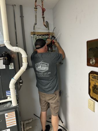 A man is repairing a furnace in a small, dimly lit room filled with tools and equipment.