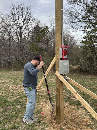 A man is climbing a pole in a grassy field, focused on his work.