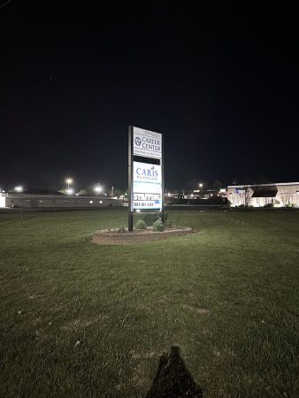 A large illuminated sign stands in a dark field at night, casting a glow on the surrounding grass.
