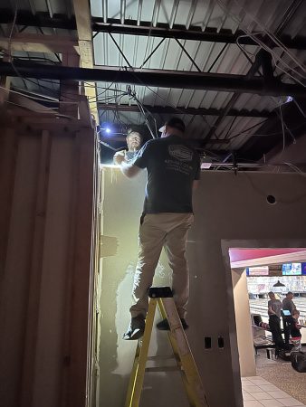 A man standing on a ladder, reaching up to work on a ceiling or overhead fixture.