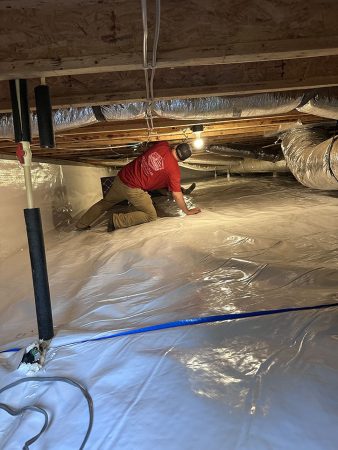 A man works on a basement floor, laying out a tarp to prepare for a project.