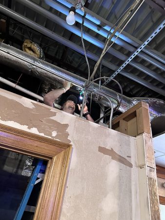 A man is repairing the ceiling in a room, using tools and standing on a ladder for better access.