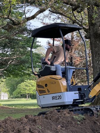 A man operates a small excavator on a construction site, focused on his task.