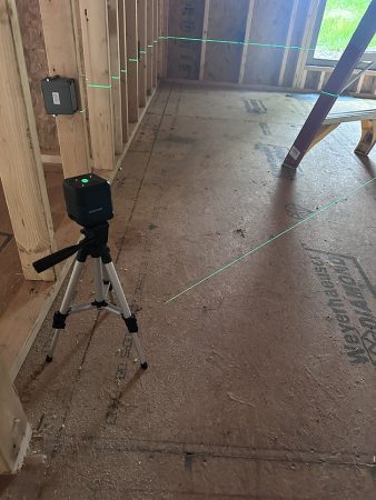 A tripod is positioned in a room, with a bright green laser beam projected across the space.