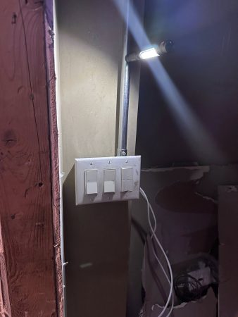 A light switch is turned on in a room with a plain wall in the background.
