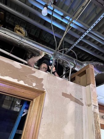 A man is repairing the ceiling in a room, using tools and standing on a ladder for better access.