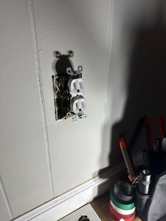 A wall outlet with a light switch above it, next to a blue toolbox on a wooden surface.
