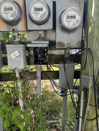 A cluster of utility meters mounted on a pole, set against a grassy field under a clear blue sky.