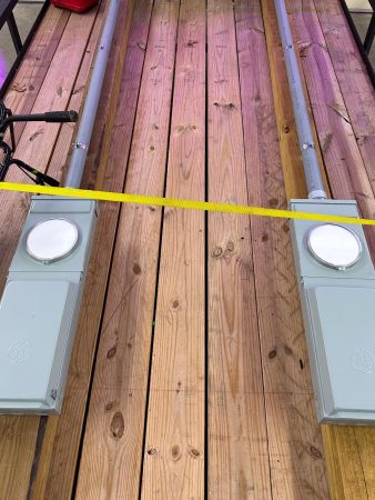 Two gray electrical boxes on wooden planks, connected by metal conduits, with a yellow caution tape across the setup.