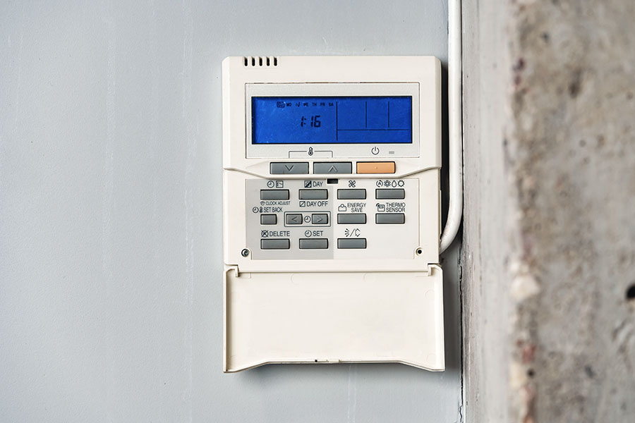 A wall-mounted programmable thermostat displaying time 1:16 with buttons for settings and adjustments.